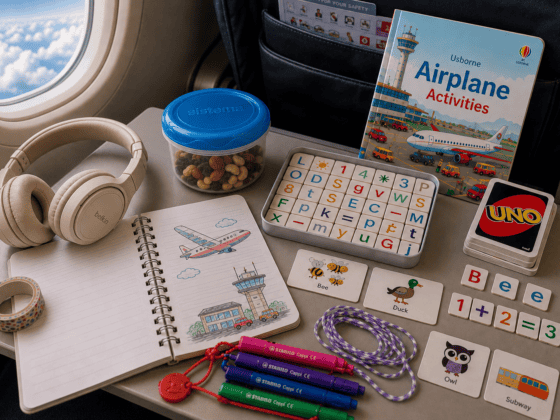 Plane activities for 5–7 year olds including Uno, letter games, notebook, Stabilo Cappi pens, Cat's Cradle string, headphones and snacks on an airplane tray table.